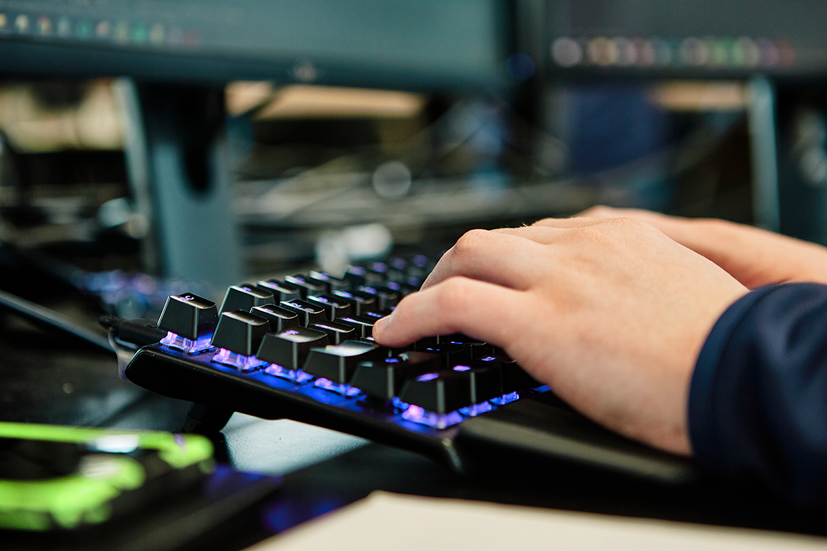 Hands typing on on a black, backlit keyboard with purple lights