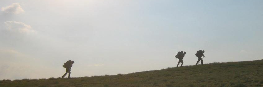 shadows of three students climb up a hill in the sun