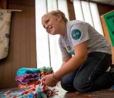 young girl on knees tying fleece blankets.