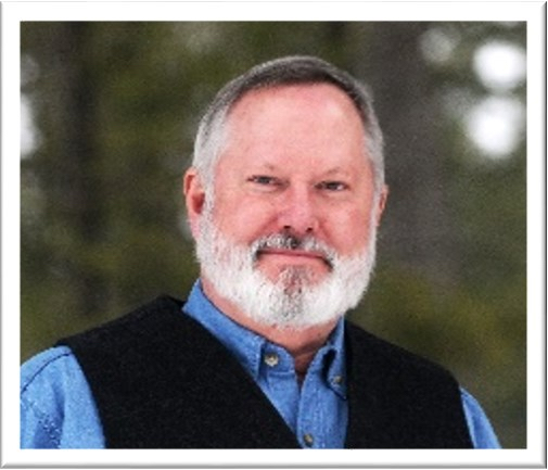 A portrait of a smiling man with a beard wearing a shirt and a vest