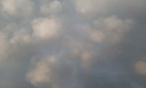 Mammatus clouds hang beneath a gray cloud layer, forming rounded, pouch-like lobes across most of the sky. The cloud bases are softly illuminated and vary in size, creating a textured appearance against a darker gray background.