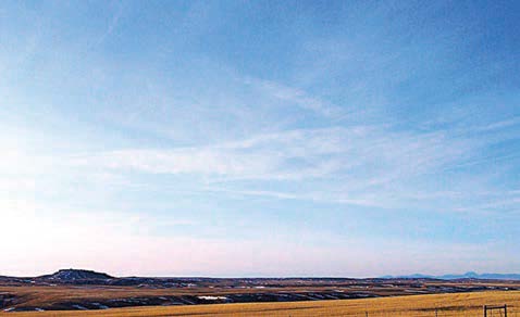 Thin cirrostratus clouds form a light, wispy veil across a blue sky above rolling grasslands and distant hills. The scene illustrates high, thin cloud layers.