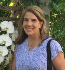 Image of Holly Mckenzie in a purple blouse next to white fowers.