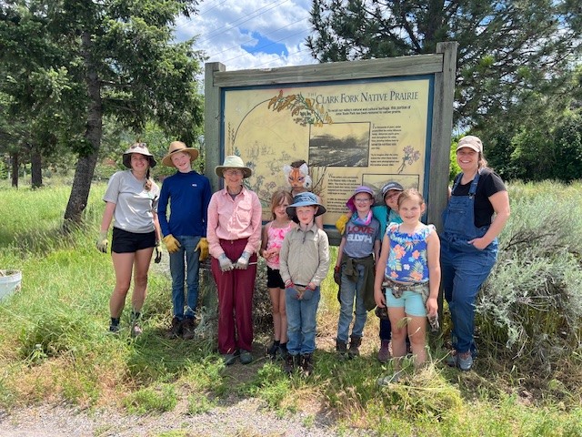 Youth and adults stand in front of a sign at the John Toole Prairie