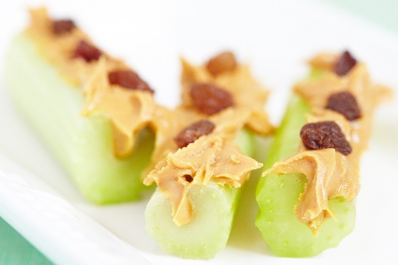 Three pieces of celery filled with peanut butter and topped with raisins.