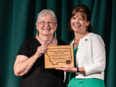 two women pose for the camera, holding up a wooden plaque together