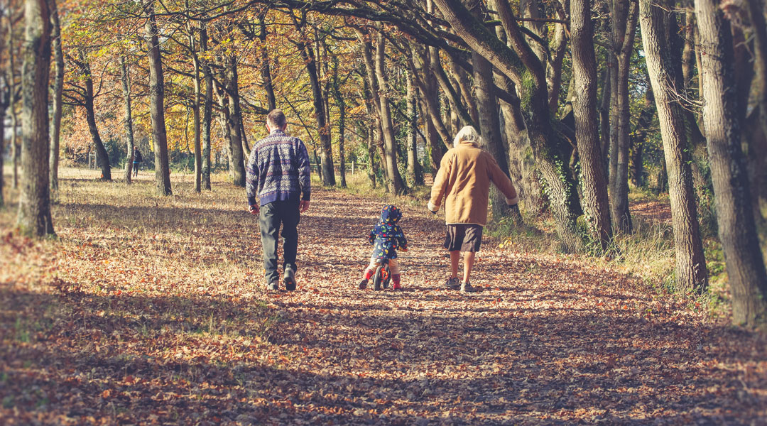 grandparents with grandchild on bike in fall leaves