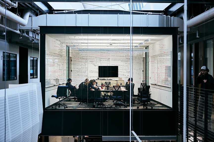 Students at a conference table in a classroom with a whiteboard wall and a mounted display