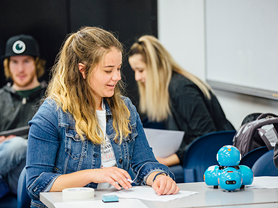 Woman with a piece of paper and a pen looking at a table-top robot