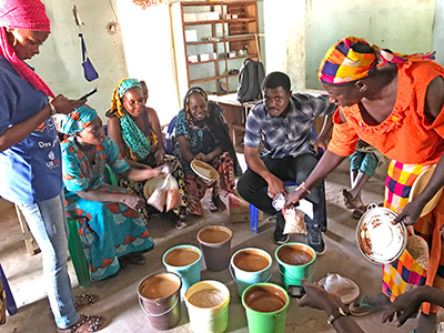 Edwin Allan and Senegalese women farmers sitting around buckets of peanut paste