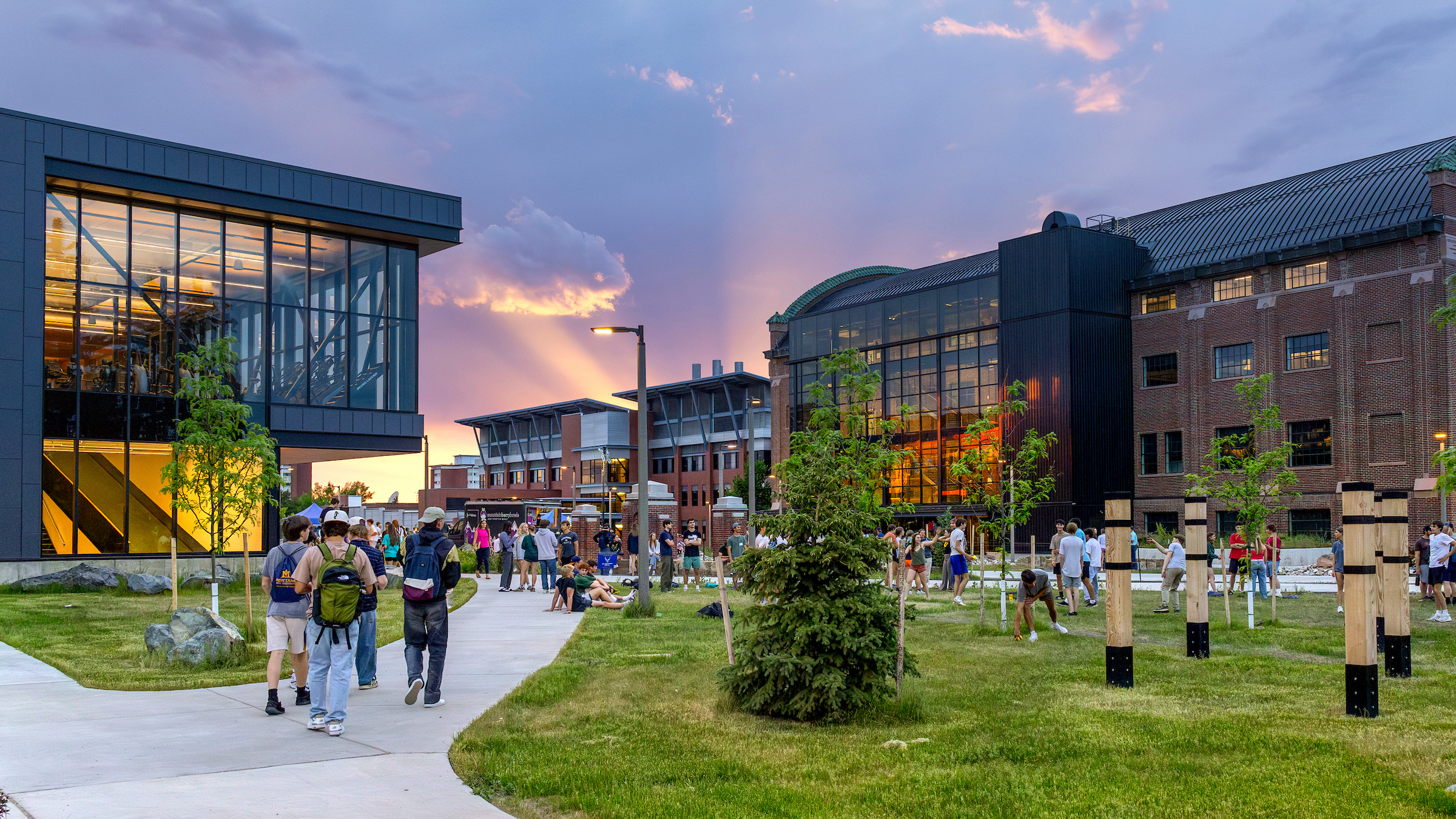 Students walking on a walkway with buildings and a sunset in the background