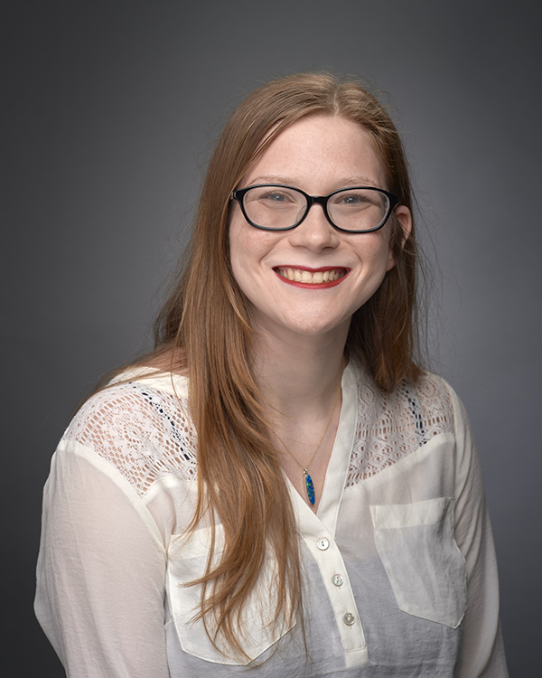 A person with long reddish brown hair wearing glasses and a white button up shirt