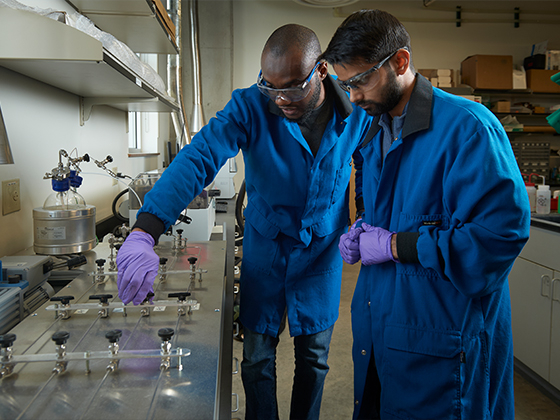 two men in labcoats with gloves and glasses