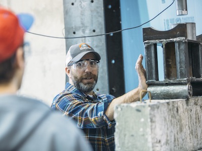 Michael Berry speaks to a student while demonstrating a concrete compression test