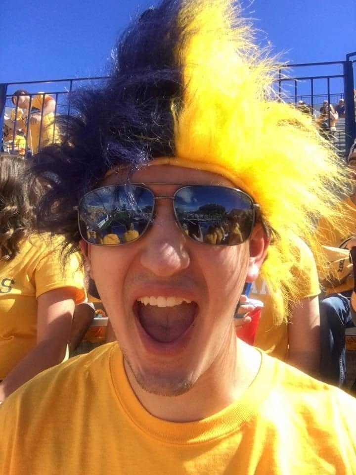 Male student wearing a crazy blue and yellow wig in the crowd at a football game