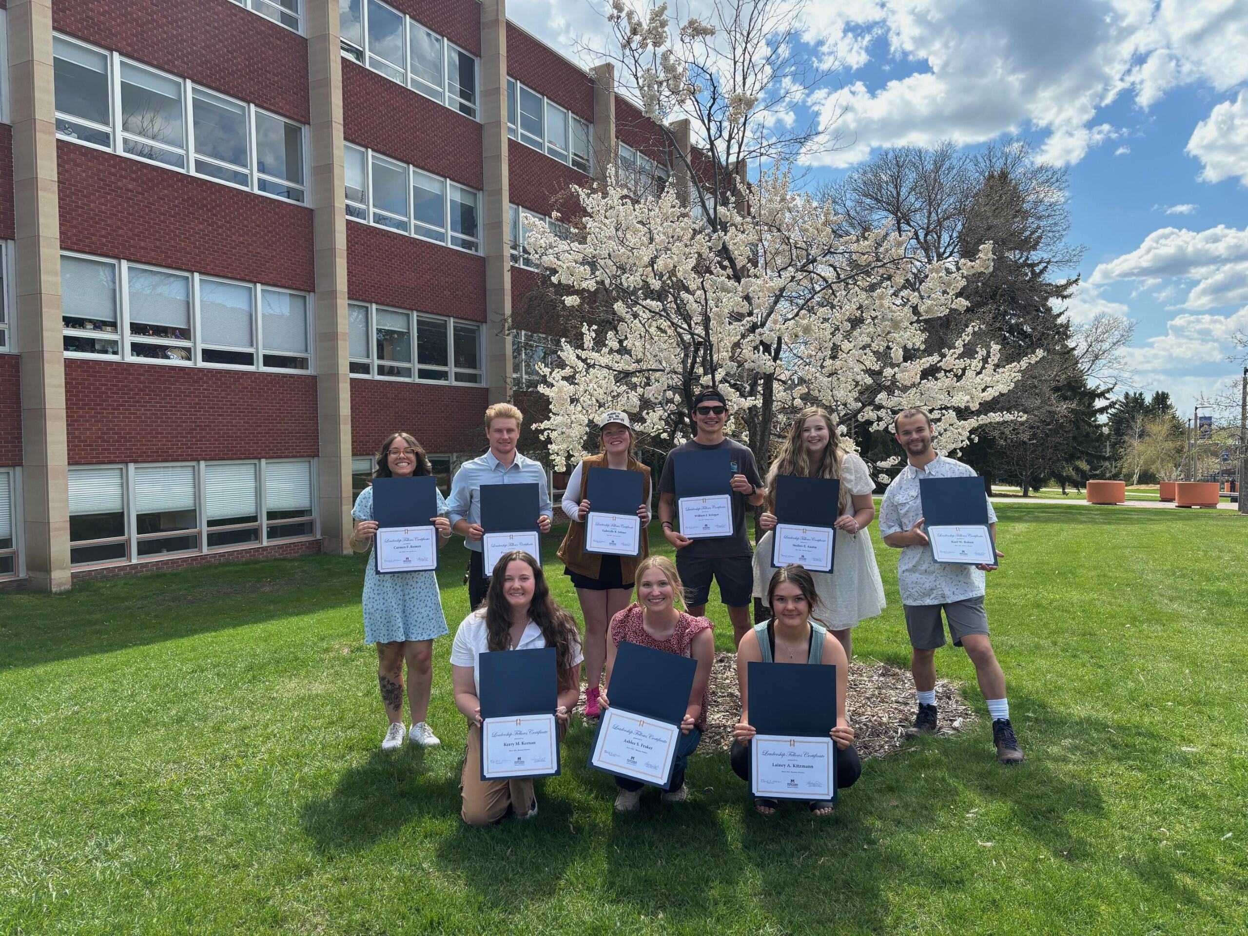 Leaderships Fellows with certificates in front of Reid Hall in spring.